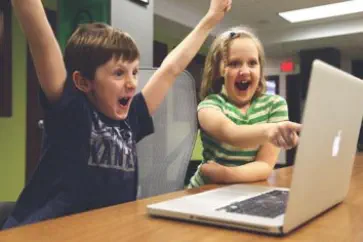 2 Kinder sieht man schreiend vor einem Laptop im Wohnzimmer